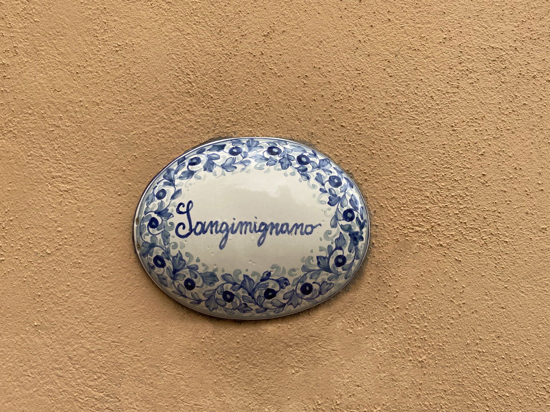 Ein dekorativer Teller mit floralen Mustern und der Aufschrift „Langimigrano“ an einer strukturierten, beigen Wand.