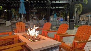 An outdoor seating area with a fire feature, chairs, and umbrellas. - Vista Cay 102 | Steps from Universal's Epic Universe & Convention Center | No Stairs, Fast Wi-Fi! (Orlando)
