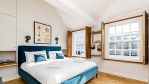 A bedroom with a large bed, wooden flooring, a window with a view, and a wall-mounted mirror. - Stunning 3BD Flat Shoreditch with Hidden Garden (London)