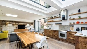 A modern kitchen with a wooden dining table, built-in appliances, and a stone accent wall. - Stunning 3BD Flat Shoreditch with Hidden Garden (London)