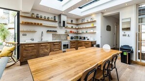 A modern kitchen with a large wooden table, built-in shelves, and a skylight. - Stunning 3BD Flat Shoreditch with Hidden Garden (London)