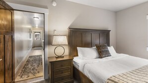 Un dormitorio con cabecera de madera, una mesita de noche con lámpara, una cama grande con ropa blanca y una alfombra estampada en el suelo.