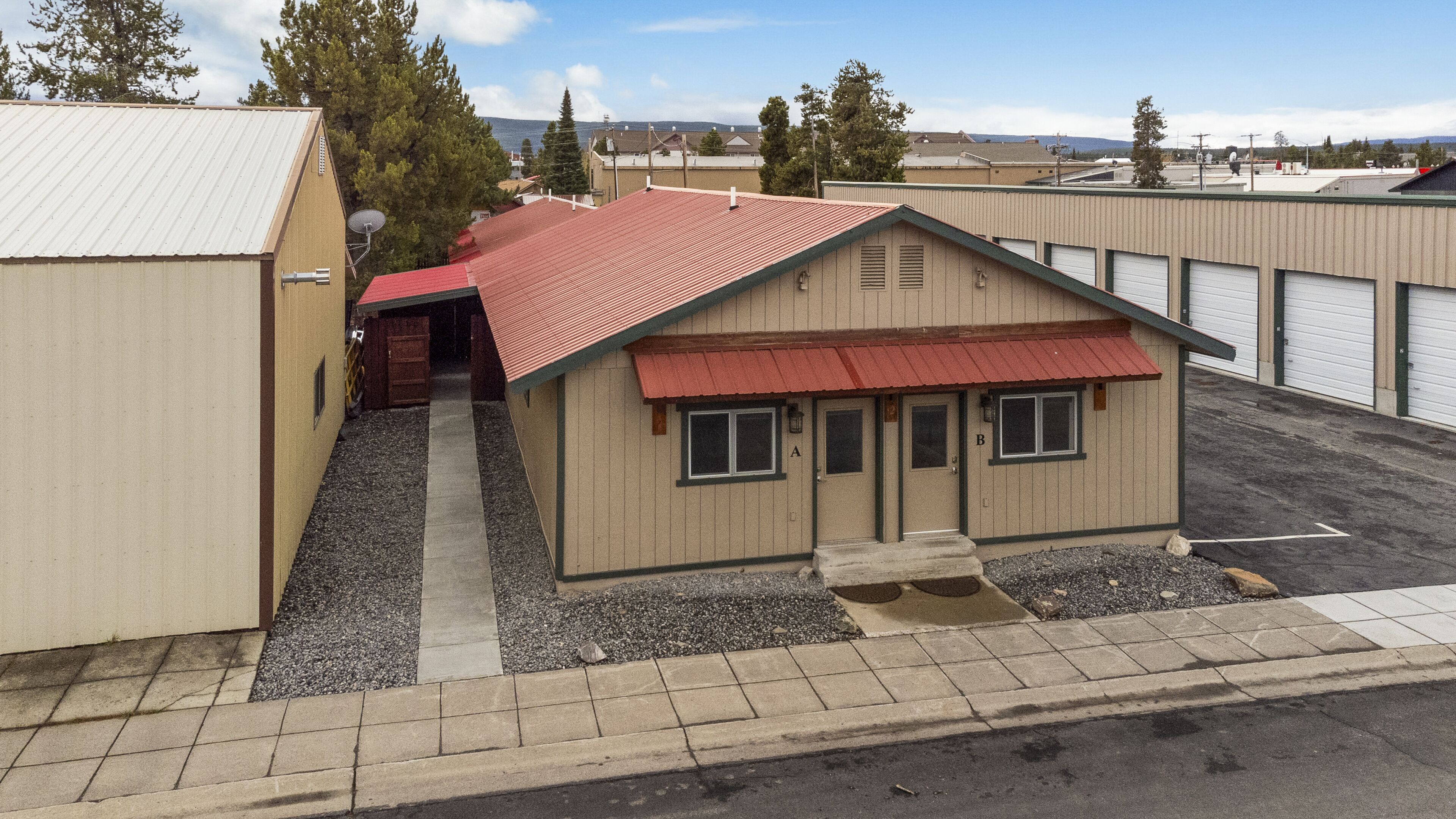 A small building with a red roof and beige walls, located in a parking lot with gravel and concrete.