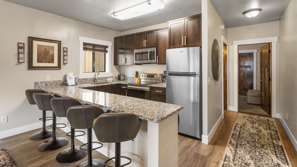 Una cocina moderna con encimeras de granito, electrodomésticos de acero inoxidable y una isla central con taburetes.