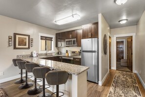 A modern kitchen with granite countertops, stainless steel appliances, and a central island with bar stools. - The Yellowstone Hideaway Unit A (West Yellowstone)