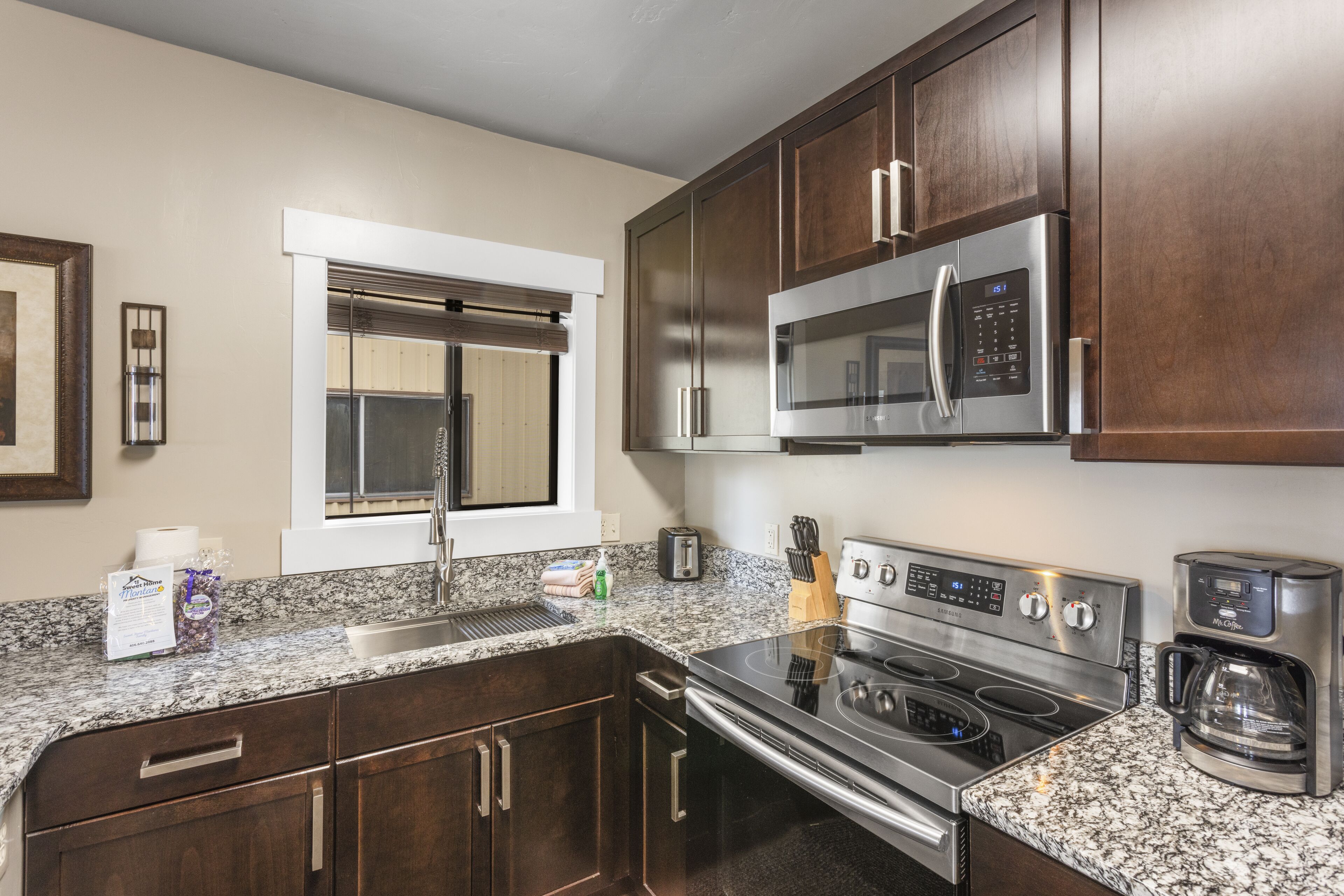A kitchen with dark wood cabinets, a stainless steel microwave, a stove, and a coffee maker.