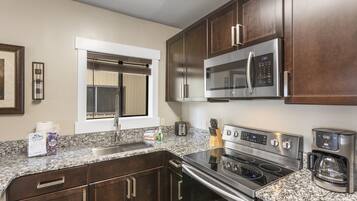 A kitchen with dark wood cabinets, a stainless steel microwave, a stove, and a coffee maker.