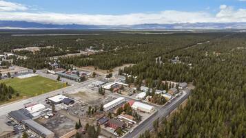 Une vue aérienne d’une petite ville où se côtoient des bâtiments résidentiels et commerciaux, le tout étant entouré de forêts denses et dominé par des montagnes en arrière-plan.