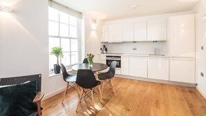 A modern kitchen with white cabinets, a round dining table with black chairs, and a wooden floor. - Fantastic 1 Bedroom Flat Leicester Square West End (Greater London)