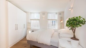 A modern bedroom with a bed, white wardrobe, and a potted plant. - Fantastic 1 Bedroom Flat Leicester Square West End (Greater London)