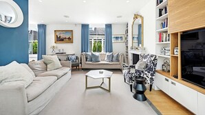 A living room with a sofa, armchair, coffee table, and a TV stand with bookshelves.