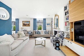 Una sala de estar con sofá, sillón, mesa de centro y un mueble para televisión con estanterías.