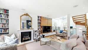A spacious living room with a fireplace, a large mirror, and a bookshelf filled with books.