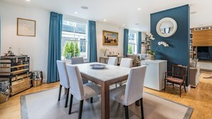 A modern living room with a dining area, a kitchen, and a large window with curtains.