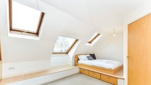 A modern bedroom with a sloped ceiling, skylights, a wooden bed, and built-in storage.
