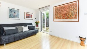 A modern living room with a black sofa, wooden flooring, and three framed artworks on the wall.