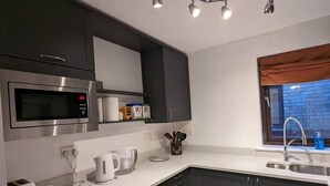A modern kitchen with dark cabinets, a built-in microwave, a coffee maker, and a window with a view of a brick building. - NEW Bright and Sunny flat in Oxford City Centre (Oxford)