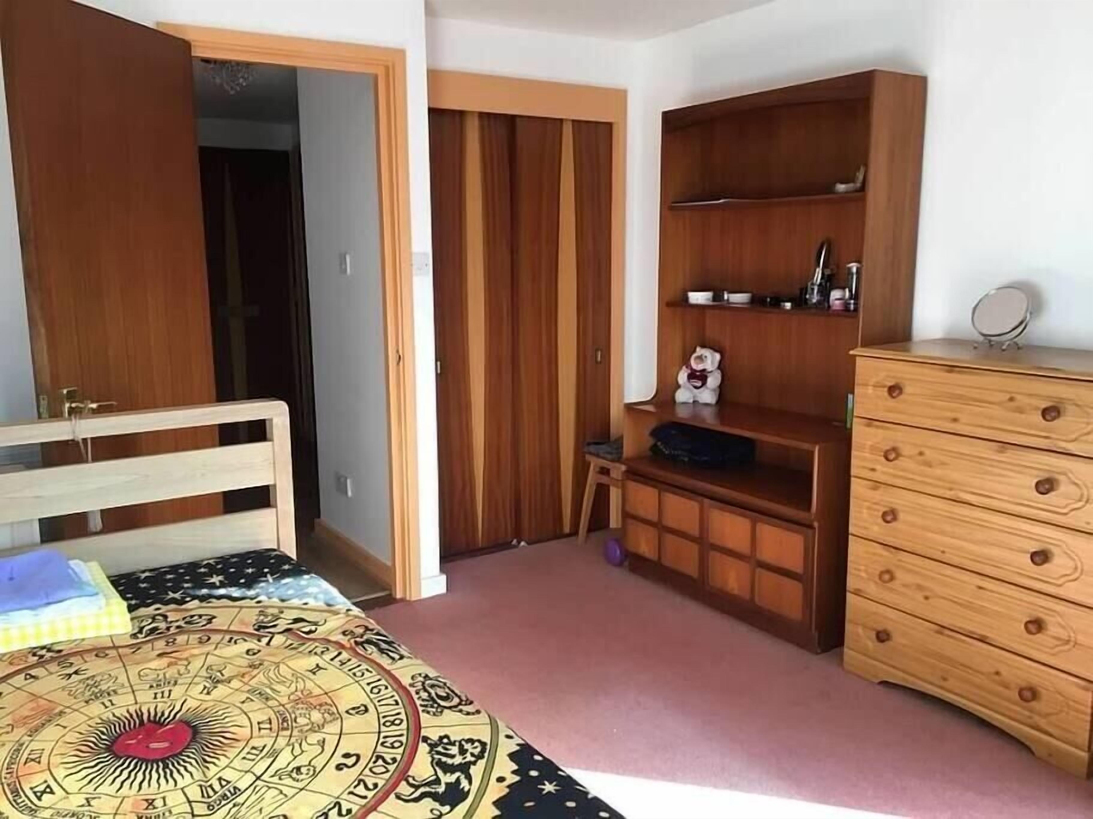 Une chambre à coucher avec un lit en bois, une armoire, une commode et un petit tabouret.