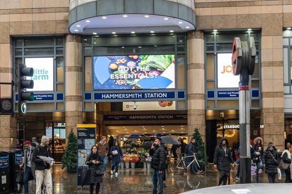 A busy urban station with a large digital advertisement for 'Got the Essentials?' and a Starbucks nearby.