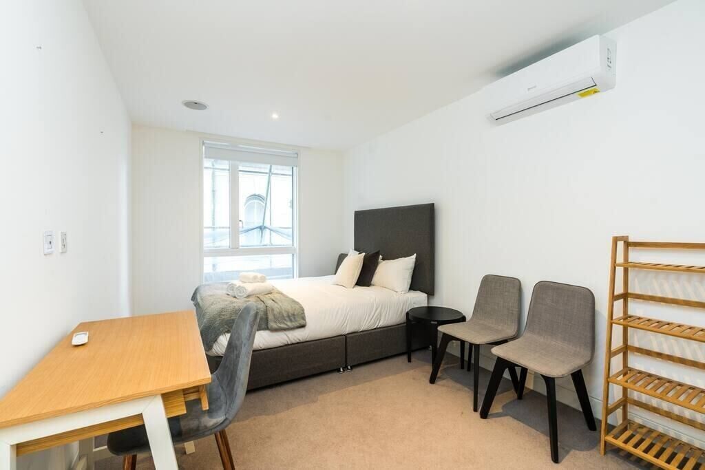 Une chambre à coucher comprenant un lit, un bureau, deux chaises, une petite table et une étagère en bois.