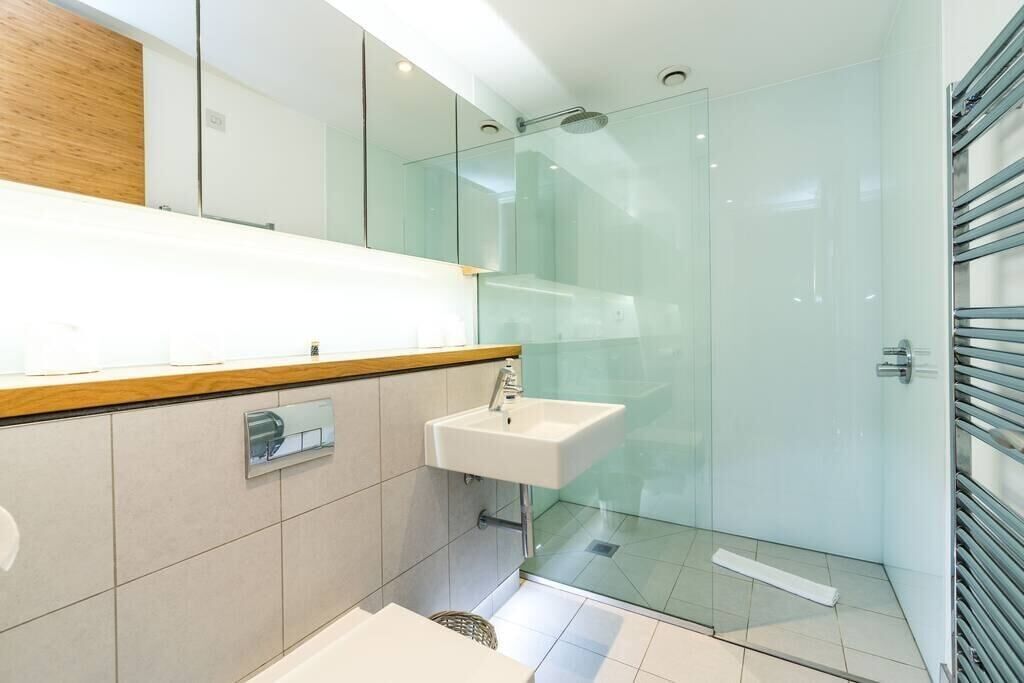 A modern bathroom with a glass shower enclosure, a white sink, and a wooden countertop.