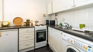Cocina compacta con muebles blancos, horno empotrado, lavadora y lavaplatos.