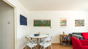 Una habitación con una mesa redonda de comedor, sillas blancas, una estantería y una silla roja.