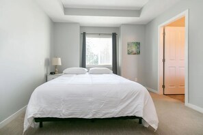 Een slaapkamer met een bed, nachtkastje, lamp, raam met gordijnen en een deur.