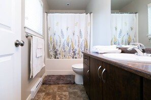 Een badkamer met douchegordijn met bloemenmotieven, toilet, wastafel met spiegel en een handdoekhouder.