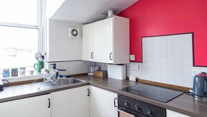 Een keuken met witte kastjes, een rode wand, een raam en een waterkoker op het aanrecht.