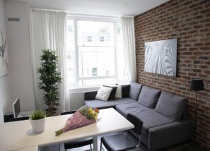 A modern living room with a grey sofa, a white table, and a potted plant.