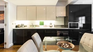 A modern kitchen with a glass dining table, black and beige cabinets, and a stainless steel range hood. - A Stunning Three Bedroom Home in Mayfair (Greater London)