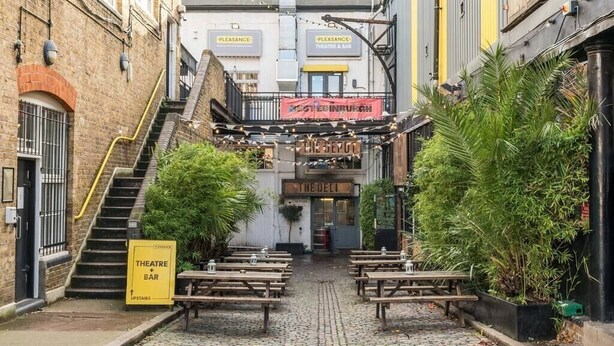 Ein Kopfsteinpflastergang mit Außenbestuhlung, einer Treppe und einem Schild für eine Theaterbar.
