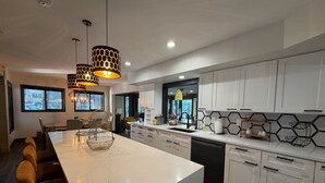 Una cucina moderna con mobili bianchi, un'isola in marmo e illuminazione a sospensione.