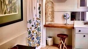 Una cocina con encimera de madera, un armario blanco, un taburete pequeño, un ventanal con marco decorativo y suelo de baldosas.