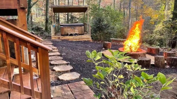 Una terraza con un pozo de fuego y un jacuzzi en un área boscosa.
