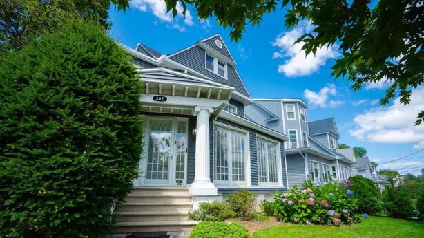 A two-story house with a large front porch, a garage, and a well-maintained lawn. - The Victorian Blue 25min to NYC (Mount Vernon)