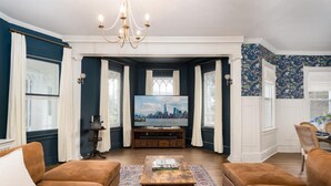 A living room with a large TV, two sofas, a coffee table, and a chandelier. - The Victorian Blue 25min to NYC (Mount Vernon)