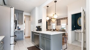 A modern kitchen with grey cabinets, a white countertop, and a built-in dishwasher. There is a coffee machine and a chandelier above the sink. - The Victorian Blue 25min to NYC (Mount Vernon)