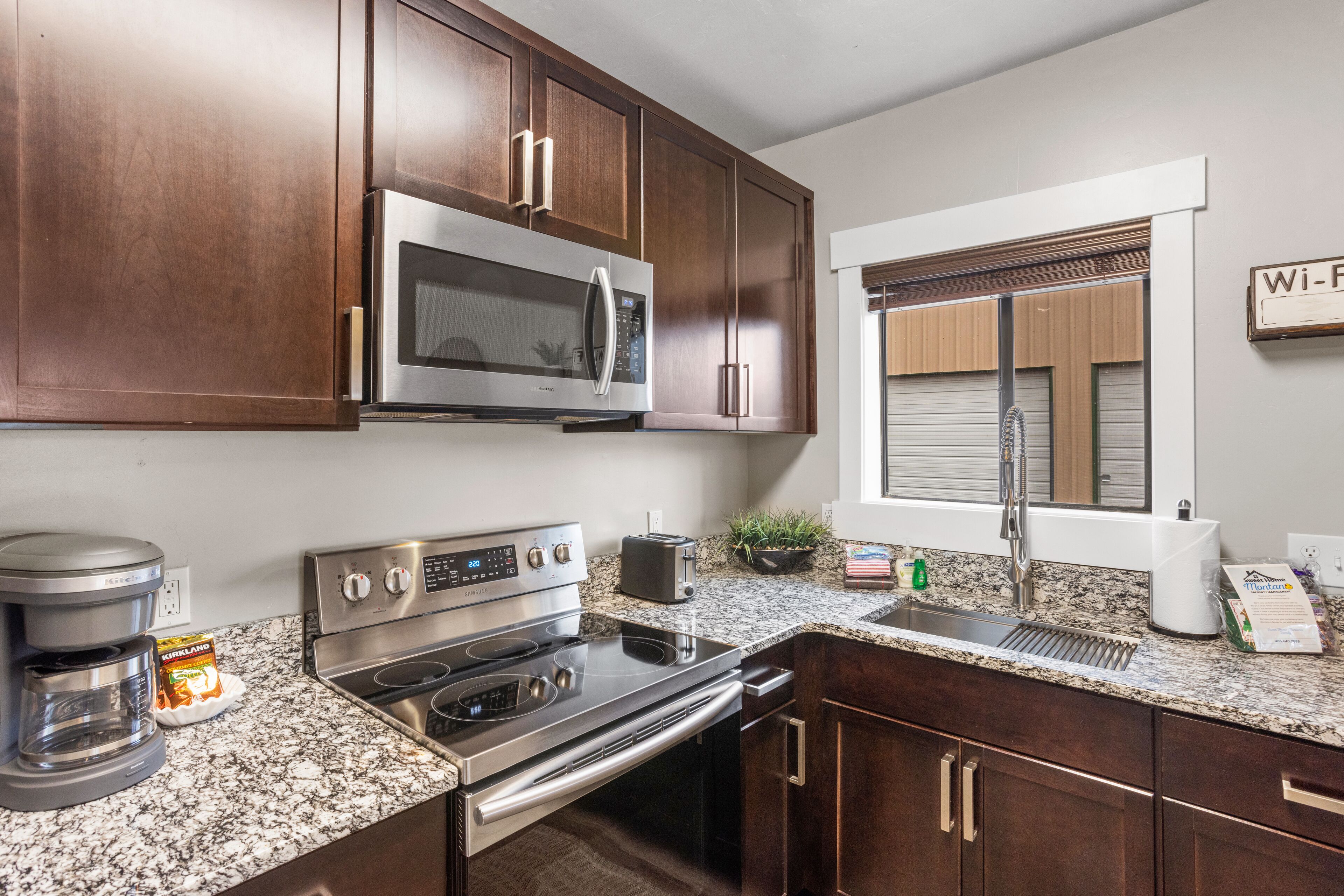 A modern kitchen with stainless steel appliances, dark wooden cabinets, and a granite countertop.