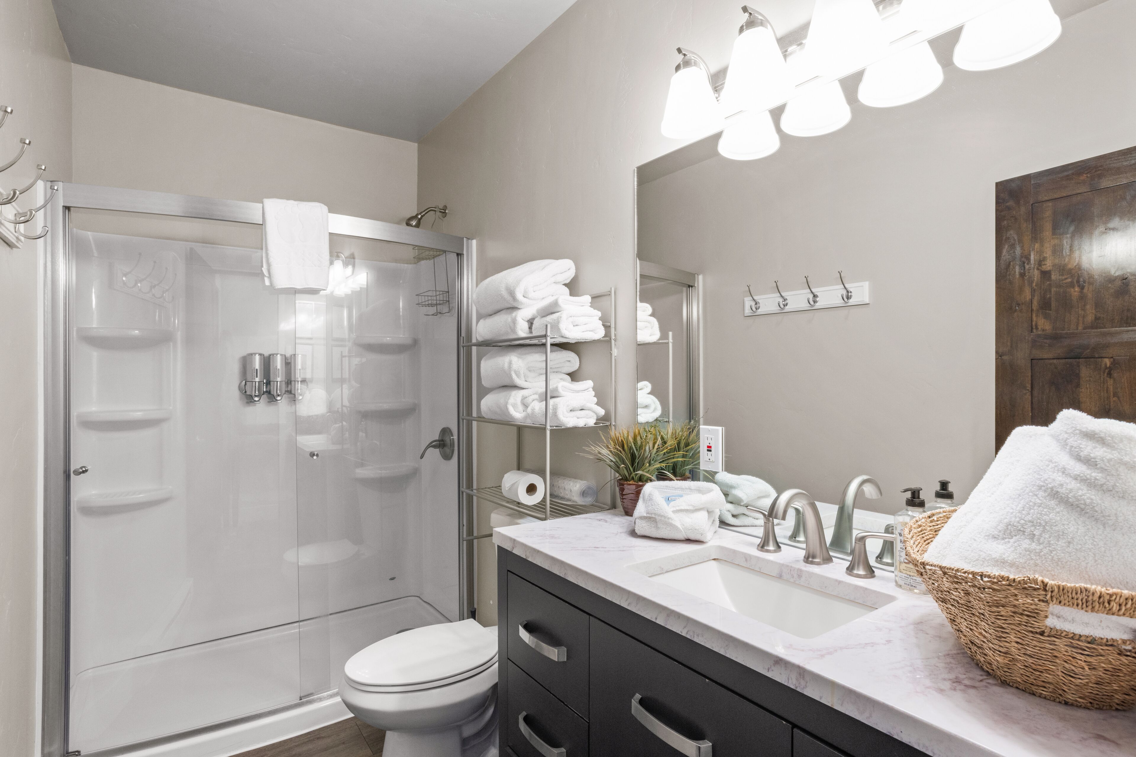 A modern bathroom with a glass shower enclosure, a white toilet, a vanity with a sink and mirror, and a towel rack with neatly folded towels.