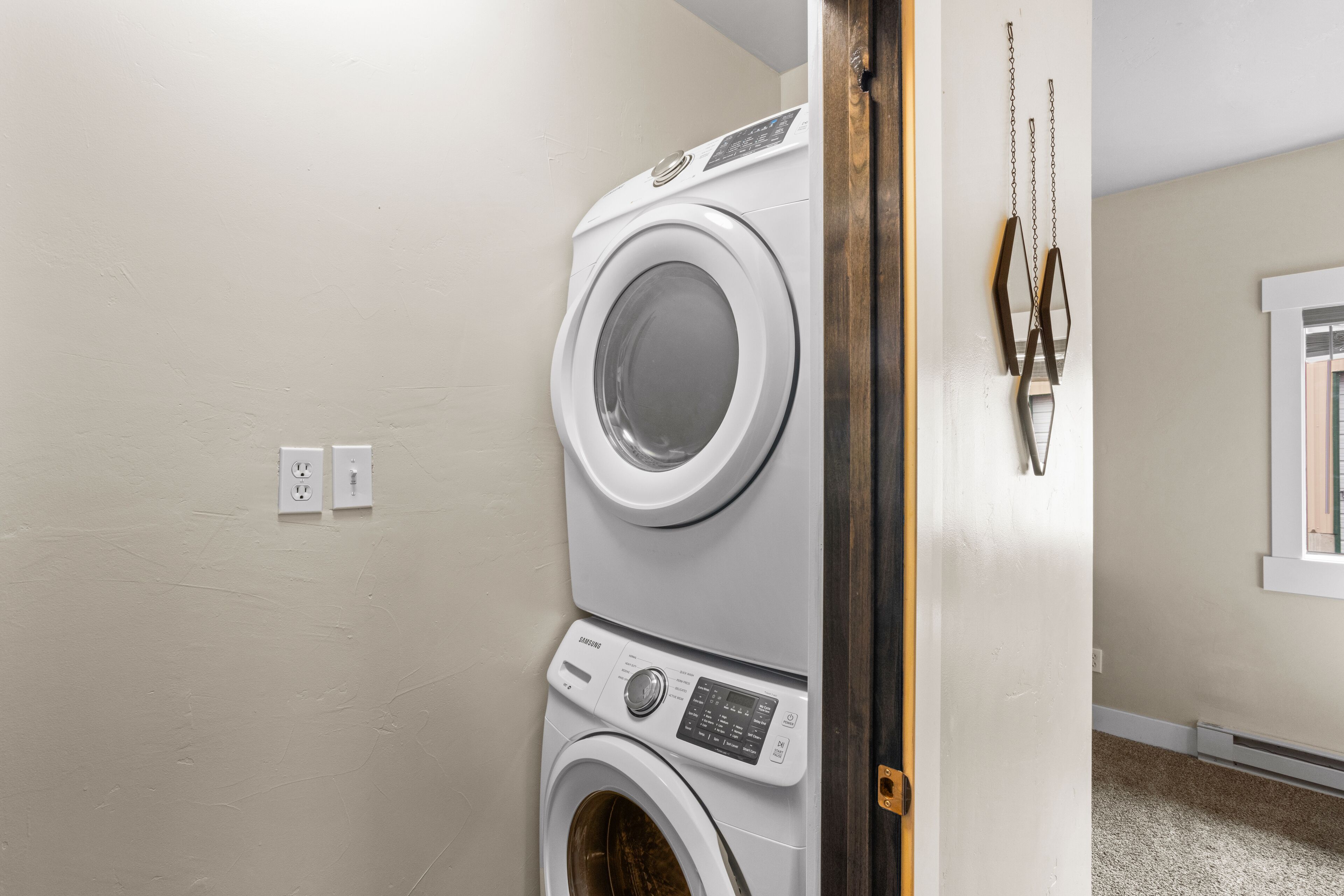 A laundry room with stacked washers and dryers, a wooden door, and a wall-mounted towel rack.