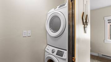 A laundry room with stacked washers and dryers, a wooden door, and a wall-mounted towel rack.