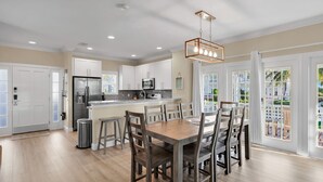 Una cocina moderna con armarios blancos, un refrigerador de acero inoxidable y una mesa de comedor de madera con sillas.