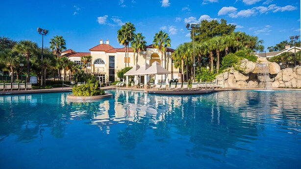 Una piscina con un edificio al fondo, palmeras y cielo despejado.