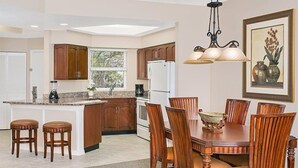 Una cocina con armarios de madera, una isla central, taburetes de bar, una mesa de comedor con sillas y una lámpara colgante.