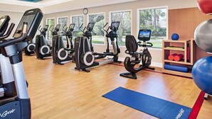 Un gimnasio con máquinas de cardio, una colchoneta azul y vistas a árboles a través de grandes ventanales.