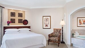 Habitación de hotel con una cama grande, una silla, una lámpara, un baño con bañera y decoración en la pared.