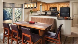 A modern kitchen with wooden cabinets, a central island, and a dining area with a bench and chairs. - Sheraton Lakeside Terrace Villas at Mountain Vista - 2 Bedroom Villa (Avon)