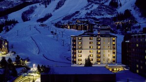 Una montaña nevada con una estación de esquí y un hotel de varios pisos y balcones.